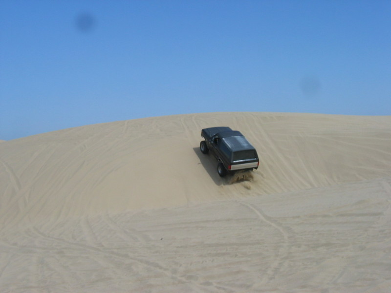 1989 Ford Bronco driving up a sand dune under a clear blue sky