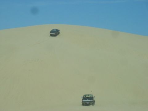 1989 Ford Bronco - Two vehicles traverse a vast sandy landscape under a clear blue sky.