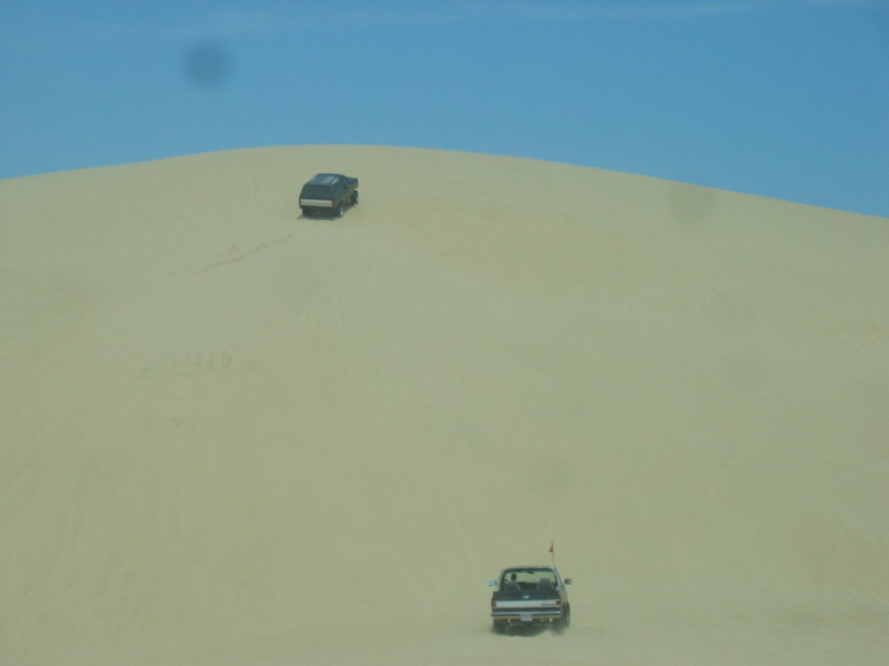 Two trucks driving on sand dunes under a blue sky
