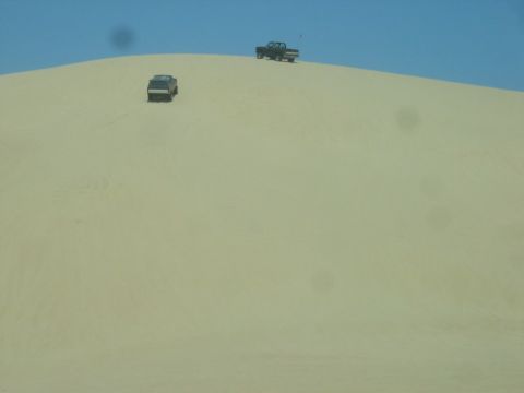 1989 Ford Bronco - Two SUVs navigate a sandy landscape under a bright blue sky.