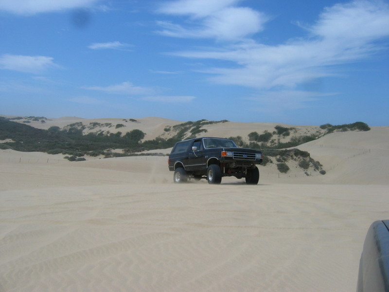 Black 1987 Ford Bronco driving on sand dunes
