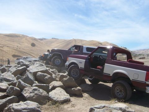 1989 Ford Bronco - Several Ford Broncos and a pickup truck tackle a challenging rocky trail on a sunny day.