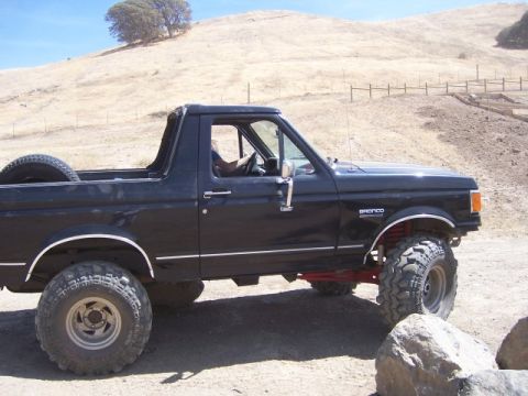 1989 Ford Bronco - A black Ford Bronco is shown from the side, parked on a dirt road with a dry, grassy hill in the background.