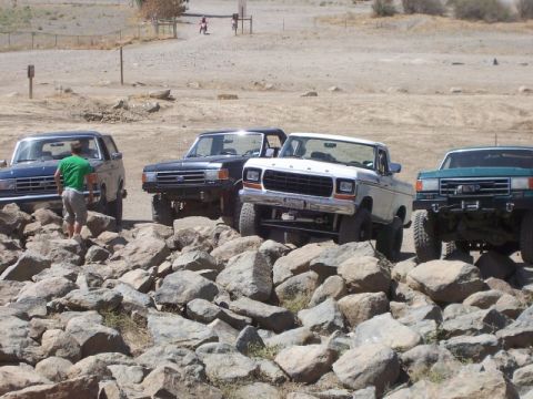 1989 Ford Bronco - Multiple trucks and SUVs are parked on a rocky terrain, with a white pickup truck prominently displayed.