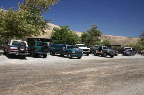 1989 Ford Bronco - A collection of SUVs and trucks are parked in a gravel lot on a sunny day.