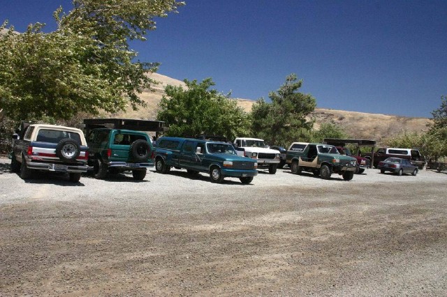Several SUVs and trucks parked in a gravel lot under a clear blue sky