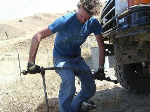 1989 Ford Bronco - A man performs maintenance on the tie rod of a truck, suggesting a model year in the 1980s based on its body style.