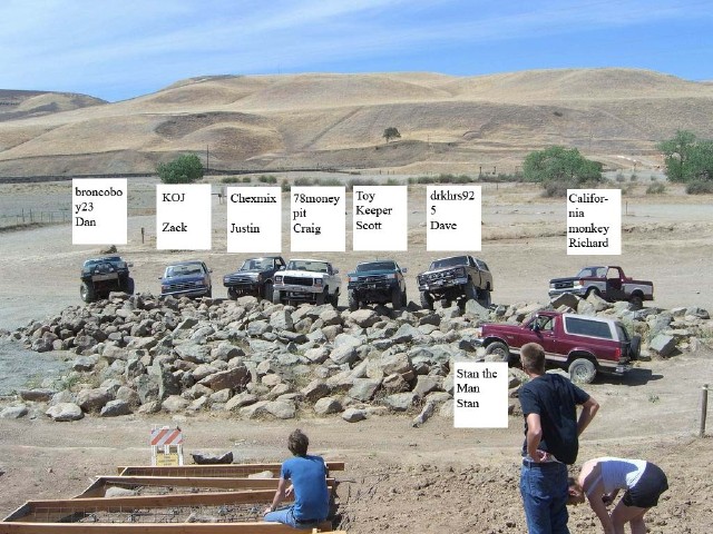 Several off-road vehicles, including a red 1989 Ford Bronco, parked on a pile of rocks with people nearby
