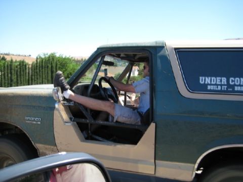 1989 Ford Bronco - A man drives a 1989 Ford Bronco with his legs extended, showing off the interior roll cage and exterior.
