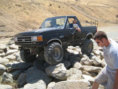 1989 Ford Bronco - Modified black Ford Bronco tackling a challenging rocky terrain during an off-road event.