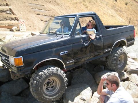 1989 Ford Bronco - A black Ford Bronco navigates a rocky obstacle course, with two occupants visible inside the cab.