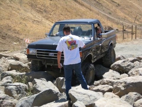 1989 Ford Bronco - A black 1989 Ford Bronco is shown maneuvering through a challenging rocky terrain during an off-road event.