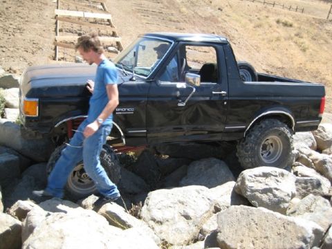 1989 Ford Bronco - Man in blue shirt stands next to a lifted black Ford Bronco on a rocky trail.