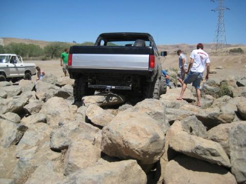 1989 Ford Bronco - A lifted Ford Bronco is shown navigating a rocky terrain with several people observing the off-road activity.