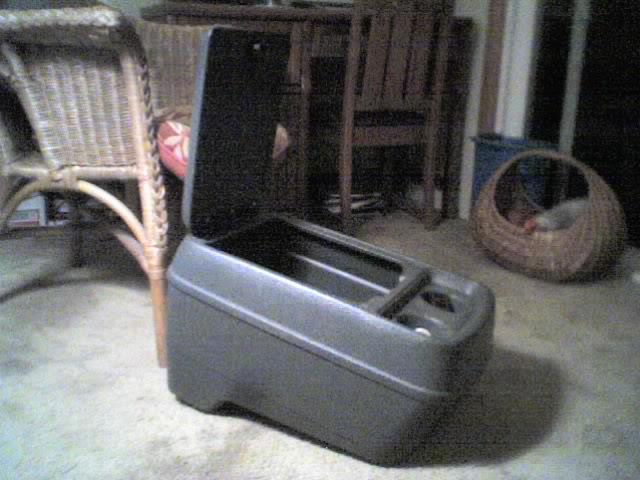 Gray plastic center console with lid open sitting on a garage floor