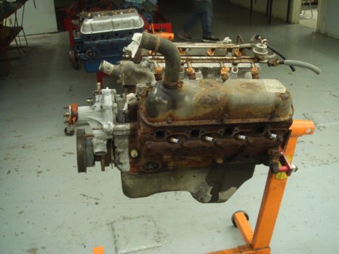 1996 Ford Bronco - A heavily rusted engine, possibly from a Ford vehicle, is displayed on an orange engine stand in a workshop.