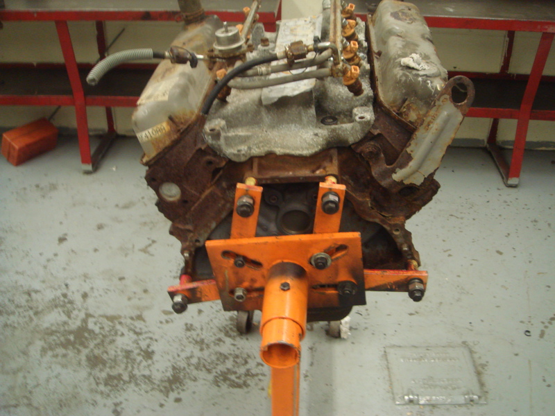 Rusty engine block on an orange engine stand, front view