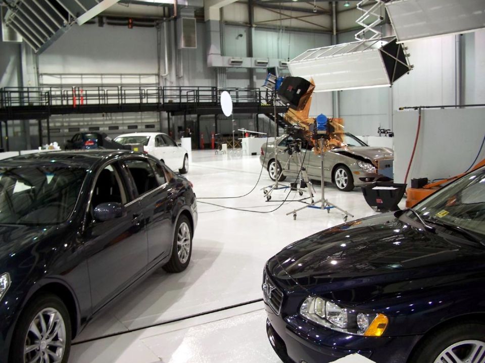 Several cars are set up in a studio with lighting equipment around them
