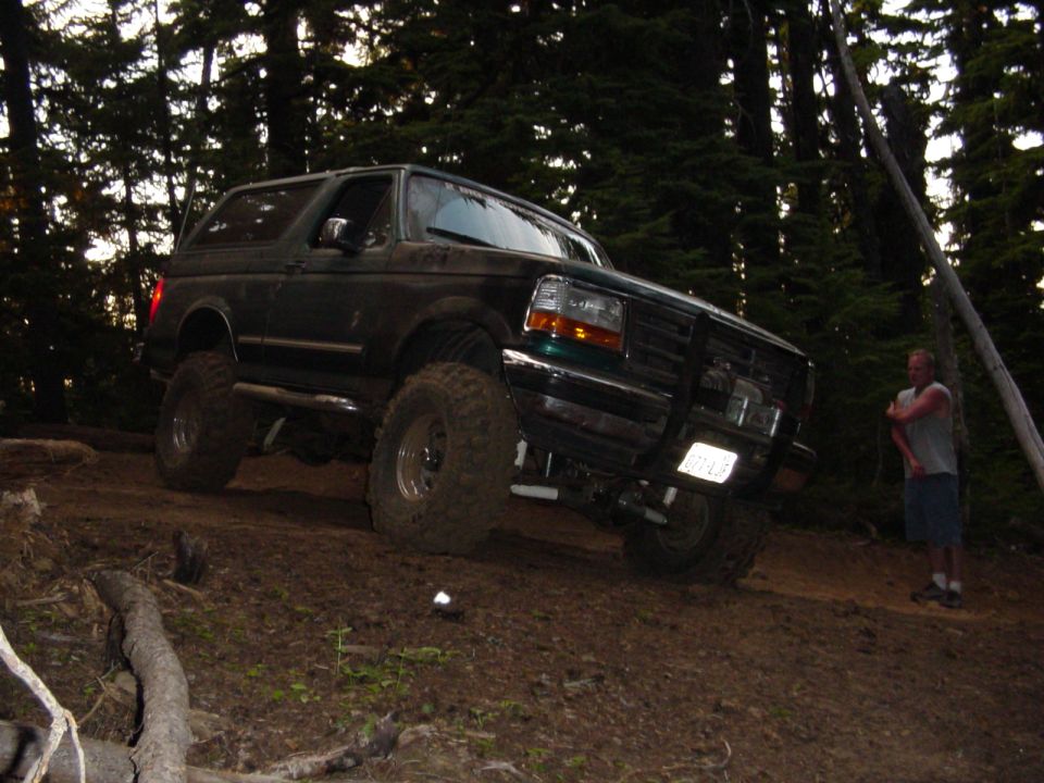 Lifted dark Ford Bronco on large tires off-road in forest at dusk