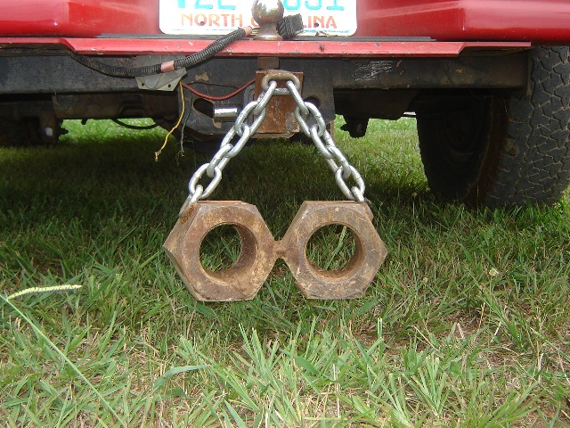 Two large rusty hex nuts hanging by chain from trailer hitch of red vehicle with NC plate