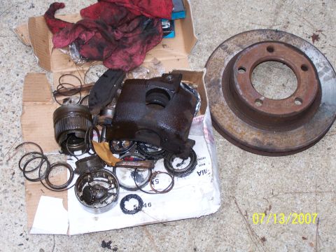 1979 Ford F-150 - A collection of brake parts, including a caliper and rotor, are laid out on the ground next to a cardboard box.