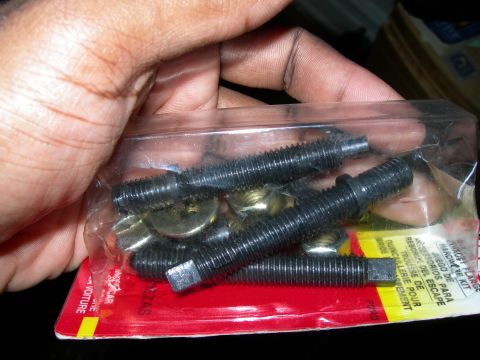 1992 Ford Taurus - Hand holds a package containing exhaust manifold studs and nuts, with visible text on the packaging.