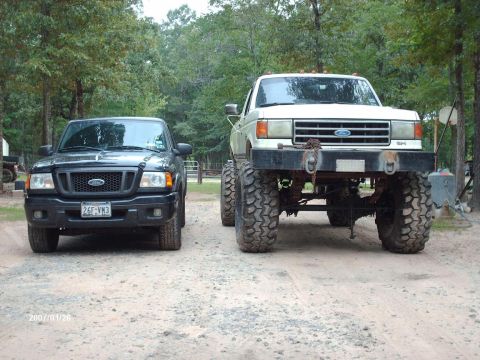 1990 Ford F-150 - A black Ford Ranger and a lifted white Ford F-Series truck are parked side-by-side on a dirt road.
