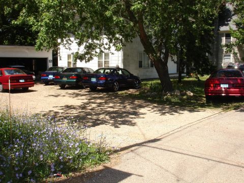 1993 Ford Taurus - Multiple sedans are parked in a gravel lot under the shade of trees.