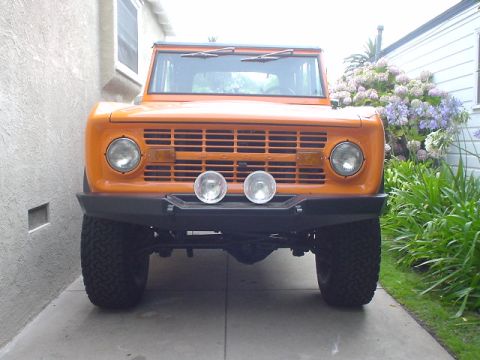 1977 Ford Bronco - Front view of an orange 1977 Ford Bronco with aftermarket bumper and auxiliary lights.