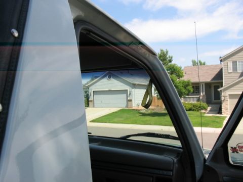 1995 Ford Bronco - View from inside a vehicle shows a suburban neighborhood with houses and garages visible through the windshield.