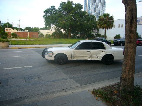 2000 Ford Crown Victoria - A damaged white 2000 Ford Crown Victoria is parked on the side of a road, showing extensive damage to its body.