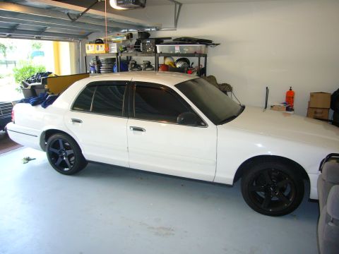2000 Ford Crown Victoria - Side view of a white 2000 Ford Crown Victoria with black aftermarket wheels in a garage.