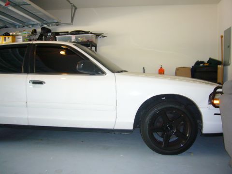 2000 Ford Crown Victoria - The side profile of a white sedan with aftermarket black wheels is visible in a garage setting.