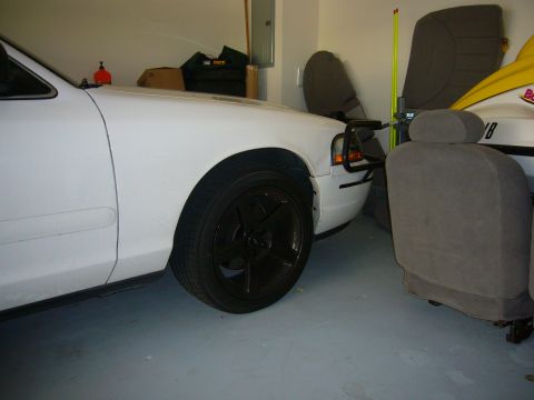 2000 Ford Crown Victoria - Front corner of a white sedan with a push bar and aftermarket wheels, parked indoors.