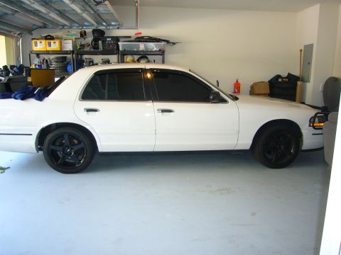 2000 Ford Crown Victoria - Side view of a white 2000 Ford Crown Victoria with tinted windows and black wheels, parked inside a garage.