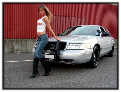 1998 Ford Crown Victoria - A woman poses next to a silver sedan with a push bar in front of a red corrugated wall.