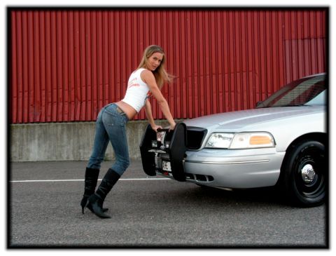 1998 Ford Crown Victoria - A woman leans on the push bar of a silver 1998 Ford Crown Victoria parked in front of a red corrugated metal wall.