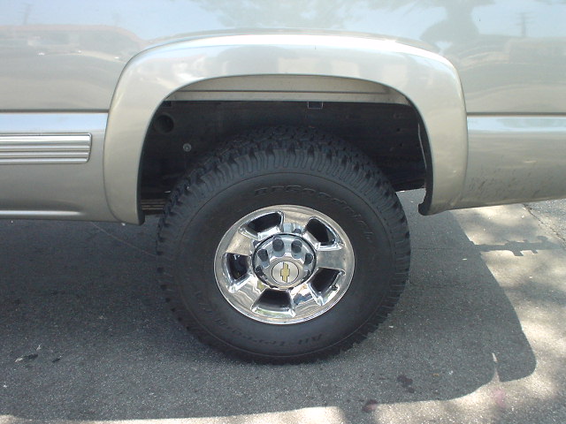 Side view of a 2002 Chevrolet Silverado 2500's rear wheel and fender. The chrome wheel has a Chevrolet badge in the center