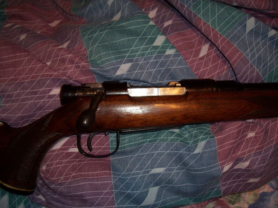 Bolt-action rifle with wooden stock and metal receiver, lying on a patterned blanket