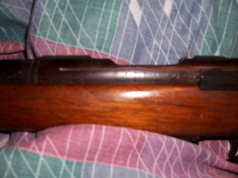 Wooden rifle receiver with visible serial numbers and metal components, resting on a patterned cloth