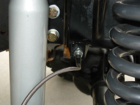 1995 Ford Bronco - Detail of suspension components, including a shock absorber and coil spring, with a braided hose visible.