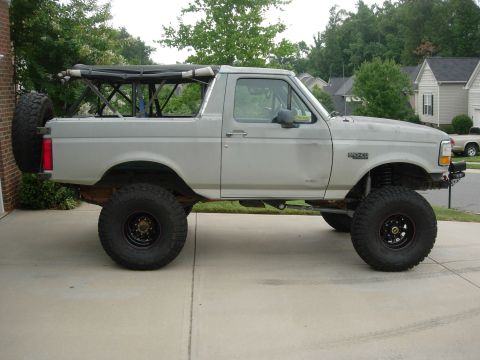 1995 Ford Bronco - Modified silver Ford Bronco with large off-road tires and a visible roll cage structure.