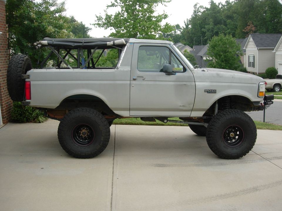 Lifted gray Ford Bronco topless with roll cage, big mud tires and rear spare carrier