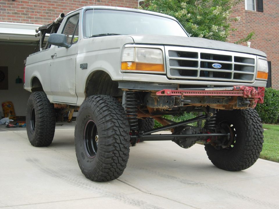 Lifted white Ford Bronco with top removed, exposed front axle and huge mud tires