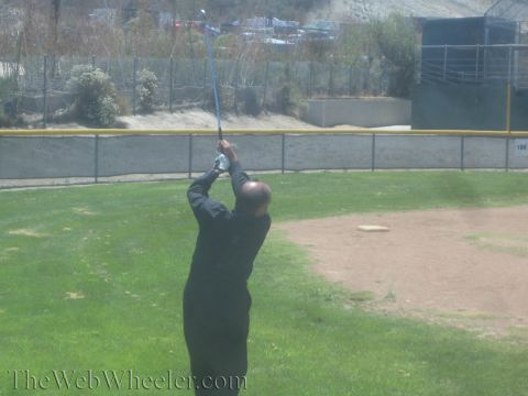 1990 Ford Bronco - man dressed in black completes a golf backswing, club raised overhead, on a grassy field beside a chain-link fence.