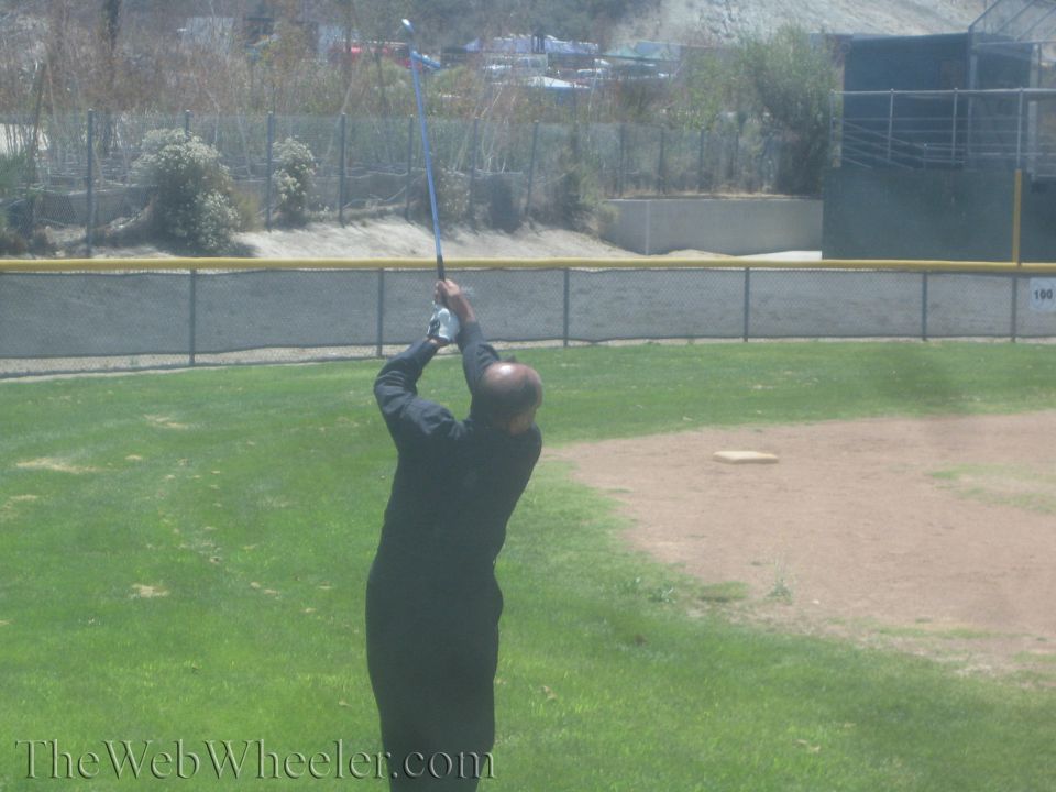 Man in black swinging a golf club at the top of his backswing on a grass field