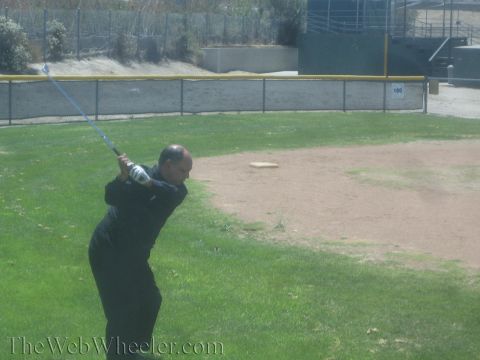 1990 Ford Bronco - man in black holds the top of his golf backswing on a grass field with a fenced backstop behind him.