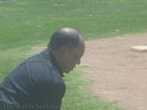 1990 Ford Bronco - bald man in a black shirt is captured in profile crouching low on a grassy field near a dirt patch.