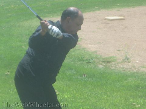 1990 Ford Bronco - gloved man in black coils through a golf swing across his body on a grass field with a base marker behind.