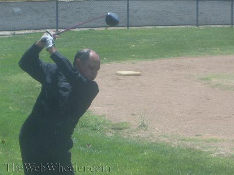 1990 Ford Bronco - bald man in black reaches the top of his golf backswing, club arced behind his head, on a grass field.